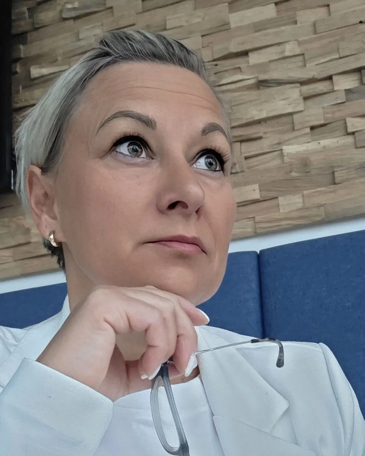 Heike Berndt im weißen Blazer, nachdenklich vor einer Steinwand